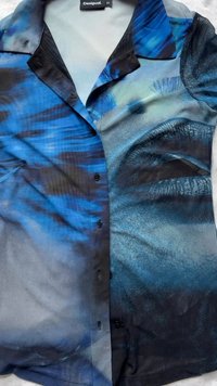Camicia a maniche corte con bottoni, caratterizzata da motivi astratti blu e neri, con una texture liscia e una vestibilità su misura. Etichetta del marchio visibile sul collo.