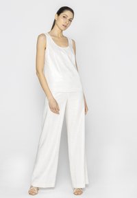 Biała bezrękawnikowa bluzka zestawiona z luźnymi, szerokimi spodniami. Materiał ma subtelną teksturę, oferując lekkie, gładkie wykończenie.