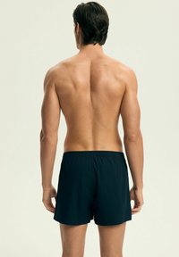 Czarne kąpielówki z elastycznym paskiem i luźnym krojem, widok z tyłu. Gładka faktura materiału i minimalistyczny design.