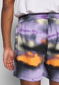Kolorowe szorty kąpielowe w wzór tie-dye, zawierające odcienie fioletu, pomarańczy i czerni. Wykonane z lekkiego materiału z elastycznym paskiem w talii.