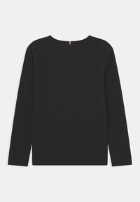 Svart langermet skjorte med rund hals. Laget av myk bomull, med en ensfarget tekstur. Baksiden har en liten detalj med røde og blå striper.