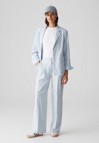Blazer taillé bleu clair et pantalons en tissu doux, complétés par un t-shirt blanc et une casquette rayée. Baskets à rayures.