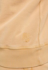 Sweat-shirt jaune avec des poignets et un ourlet côtelés. Présente un logo "PULL IN" brodé en bas. Texture douce, design décontracté.