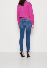 Sudadera rosa corta combinada con jeans ajustados azules; los jeans tienen bolsillos traseros y un lavado claro; el modelo lleva tacones negros.