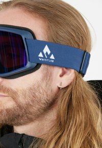 Snowboardlasit, joissa on sininen hihna valkoisella "WHISTLER"-logolla, tummat linssit ja mustat vaahtomuovipehmusteet. Suunniteltu lumilautailun käyttöön.