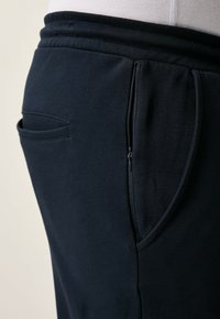 Marina blå sweatpants tillverkade av mjukt tyg med en välsittande midja, med en sidoficka med dragkedja och en klassisk passform.