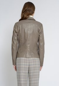 Läderblazer i taupe, figursydd design med en mjuk textur, notchkrage och knappmanchetter, i kombination med rutiga byxor.
