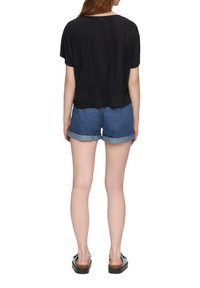Schwarzes, plissiertes Kurzarmoberteil, kombiniert mit Jeansshorts. Die Shorts verfügen über umgeschlagene Säume und einen lässigen Schnitt, der durch schlichte Schuhe hervorgehoben wird.
