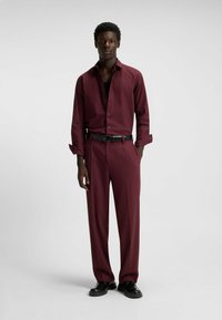 Maroon shirt with open collar and long sleeves, paired with matching maroon trousers and a black belt. Smooth fabric, tailored fit.