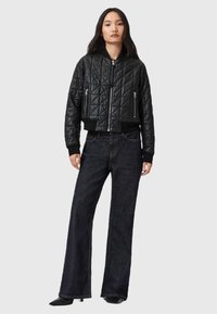 Zwarte gewatteerde bomberjack met een aansluitende tailleband, twee ritszakken en ribgebreide manchetten. Gecombineerd met wijde, donkere spijkerbroeken.