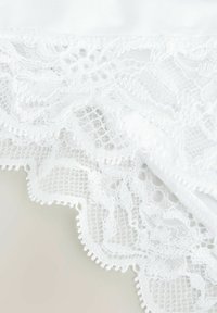 Witte lingerie met een delicate kantafwerking met ingewikkelde bloemenpatronen en gegolfde randen, gemaakt van gladde, lichte stof.
