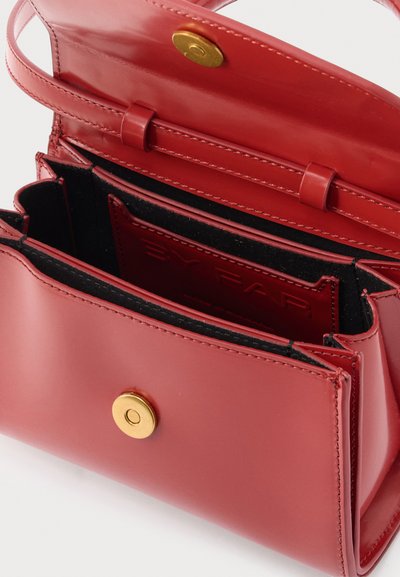 Červená kožená kabelka so zlatým magnetickým zámkom, otvoreným klapkovým vekom a viacerými vnútornými priehradkami vrátane priehradky na značkovú kartu.