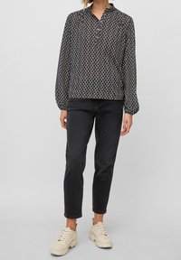Blusa nera con motivo a fiori bianchi, colletto e maniche lunghe a sbuffo, abbinata a jeans neri e sneakers chunky beige.