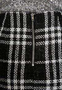 Falda de cuadros en blanco y negro con un acabado texturizado, que presenta un cierre de cremallera metálica. La parte superior tiene brillantes lentejuelas.