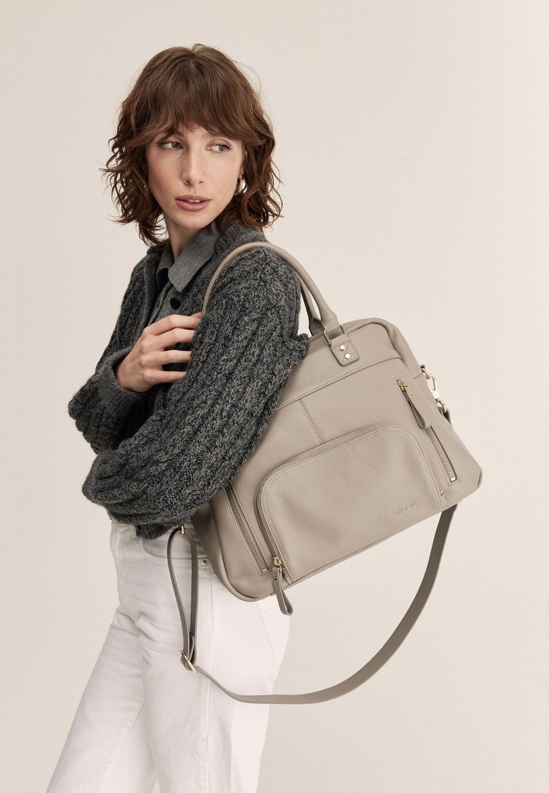 Borsa a mano grigia in pelle con due tasche con zip, manici corti e tracolla regolabile. Texture liscia e design minimalista.