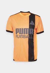 Puma fotbollströja i orange och svart, med horisontella ränder, rundad halsringning och en stor grå logo på framsidan.
