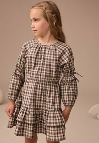 Abito a pois beige e nero con maniche a sbuffo, vita elastica e orlo arricciato. Realizzato in tessuto morbido con dettagli in nastro.