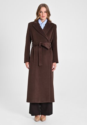 Cappotto lungo marrone con vita a cintura, realizzato in tessuto morbido, con colletto a rever e maniche lunghe complete, abbinato a pantaloni neri a gamba larga.
