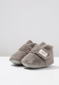Een paar zachte, grijze UGG babybooties met klittenband en een luxe textuur, tentoongesteld op een witte ondergrond tegen een lichtgrijze achtergrond.
