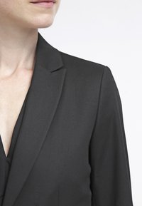 Svart kavaj med en strukturerad krage, slät textur och en figursydd design, som visar endast den övre delen och nackområdet.