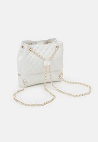 Vit kviltad bucketväska gjord av konstläder, med guldiga kedjehandtag, dragsko-stängning och ett ficka med dragkedja i botten.