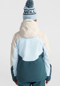 Veste à trois tons bleu clair et turquoise avec capuche, en matière lisse ; arbore le logo O'Neill au dos et un bonnet bleu assorti avec pompon.