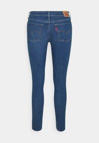 Jeans de denim azul ajustados con una textura suave, que cuentan con un parche de cuero en la cintura y dos bolsillos traseros con un diseño bordado.