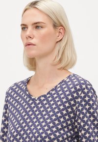 Marinblå mönstrad topp med V-hals, korta ärmar och ett geometriskt mönster i kräm. Mjuk tyg med en slät yta.