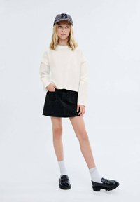 Bijela dugački rukavi crop top, crna traper suknja, sivi čarape i crni mokasini. Kapa ima uzorak `houndstooth` s logom.