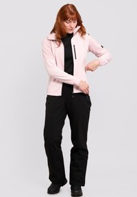 Veste en polaire zippée rose clair avec un col haut, design ajusté et une poche zippée à l'avant. Associée à un pantalon noir et des bottes.