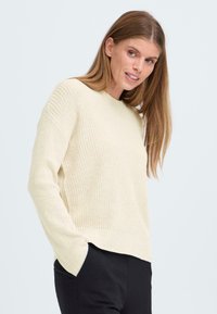 Maglione di cotone leggero con scollo rotondo, texture a coste e spalle scese. Abbinato a pantaloni neri, che mostrano un fit rilassato.