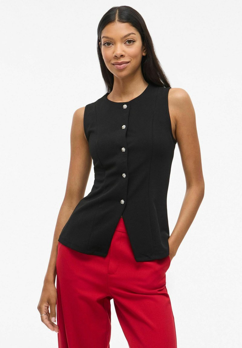 Svart ärmlös topp med rund halsringning, med en knappslå framtill med klara, dekorativa knappar. Tyget ser slätt och figurnära ut.