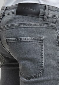 Gros plan d'une personne portant un jean gris avec une étiquette en cuir noire cousue au-dessus de la poche arrière.