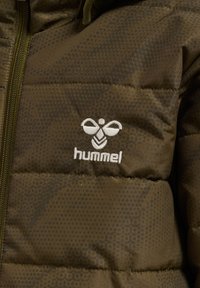 Pikowana kurtka w kolorze oliwkowej zieleni z kropkowaną fakturą, z zamkiem błyskawicznym z przodu i białym wyszywanym logo "hummel" na lewej piersi.