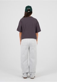 Tmavě šedé oversized tričko s krátkým rukávem, spárované se světle šedými tepláky. Oblečení doplňuje zelená kšiltovka.