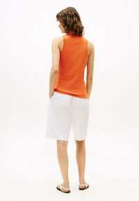 Pomarańczowa koszulka bez rękawów, białe szorty i sandały. Strój ma gładką teksturę, luźny krój i boczne kieszenie w szortach.