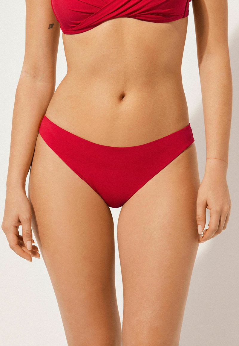 Bas de bikini rouge en tissu lisse. Le design présente une taille basse avec des bords nets et une couverture minimale sur les côtés.