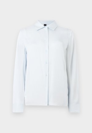 Chemise blanche à manches longues avec col pointu et poignets, présentée sur un fond clair uni.