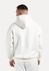Hvid hoodie med en stor hætte, der har en glat tekstur, ribbede manchetter og et let drop-skulderdesign. Minimalistisk æstetik.
