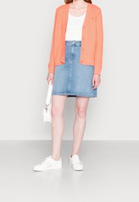 Korálový pletený kardigan, bílý tílko, modrá denimová sukně a bílé tenisky. Minimalistický design, přiléhavý střih, hladká textura, ležérní vzhled.