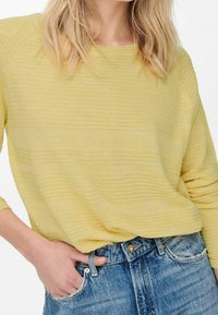 Pull tricoté jaune texturé à coupe décontractée et manches trois-quarts, assorti à un jean en denim bleu clair taille haute.