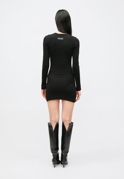 Czarna mini sukienka z długim rękawem o dopasowanym kroju, gładkiej fakturze i okrągłym dekolcie. Do tego czarne kozaki za kolano z wycięciami w kształcie litery V.