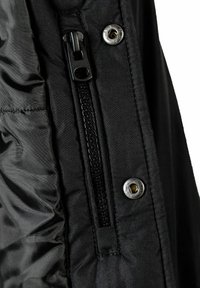 Tissu de veste noire avec une fermeture éclair, des fermetures à pression et une doublure texturée avec des détails de couture. Gros plan sur la zone de fermeture.