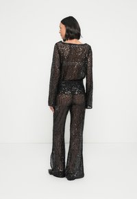 Combinaison noire à sequins avec manches longues et pantalons larges. Tissu transparent mettant en valeur la silhouette en dessous, complété par une coupe ample.