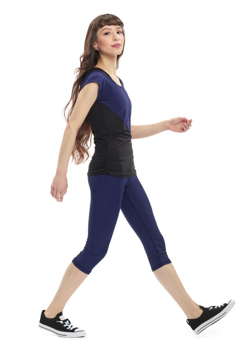 Blue and black activewear set featuring a fitted top with short sleeves and ruched detail, paired with knee-length leggings and black sneakers.