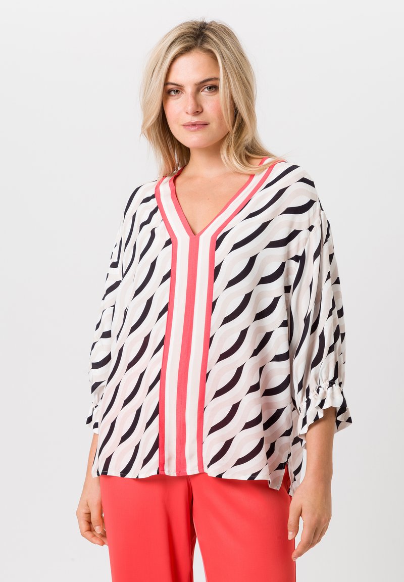Blouse ample blanche avec un motif en vagues noires, dotée d'un col en V et d'accents rayés rouges. Tissu doux avec des détails de manches nouées.