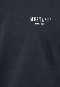Tamsiai pilka medvilninė marškinėliai su baltu "MUSTANG" logotipu ir užrašu "SINCE 1932". Savybės: lygi tekstūra ir apvalus kaklo iškirptis.