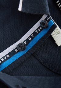 Jūras flotes polo krekla apkakle ar teksturētu virsmu, ar zilu un baltu svītru. Ietver melnu pogu un izšūtas birkas zīmola identifikācijai.