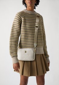 Malá crossbody taška v krémové barvě s opakujícím se vzorem loga. Má hladkou strukturu, nastavitelné uško a kovové akcenty.