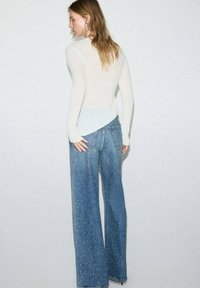 Suéter de punto ajustado en azul claro, con mangas largas, combinado con jeans de pierna ancha en azul claro que presentan un patrón sutil y un dobladillo deshilachado.